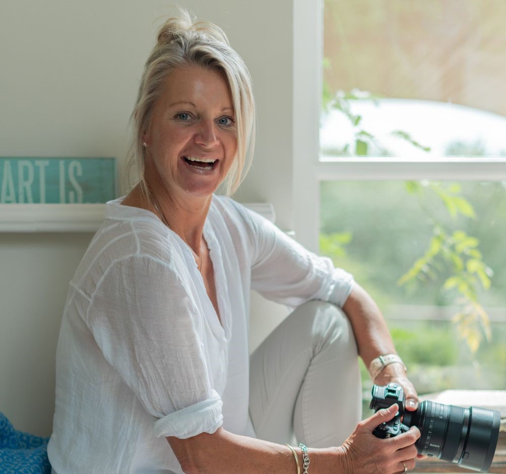 a woman holds her camera and smiles during a personal brand photography shoot in guildford
