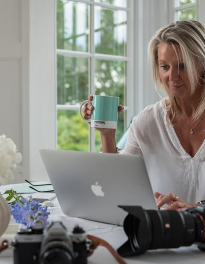 a woman sits at her desk in a sun filled room during a personal brand photography shoot in guildford