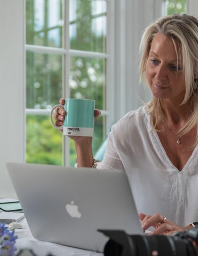 a woman sits at her desk in a sun filled room during a personal brand photography shoot in guildford