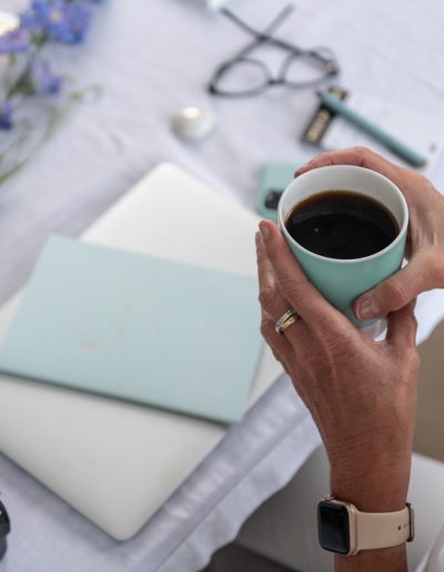 a woman holding a cup of coffee at her desk during a personal brand photography shoot in surrey