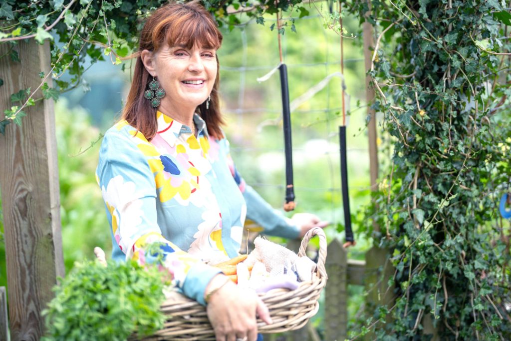 a young woman holding a basket of vegetables from her garden during a personal brand photography shoot in guildford