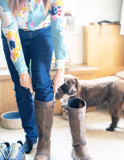 a woman pulls on her riding boots whilst her dog looks on during a personal brand photography shoot in surrey
