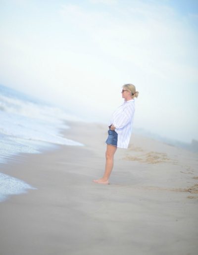 a woman stands on a beach looking out to see in the Hamptons during a lifestyle photography shoot