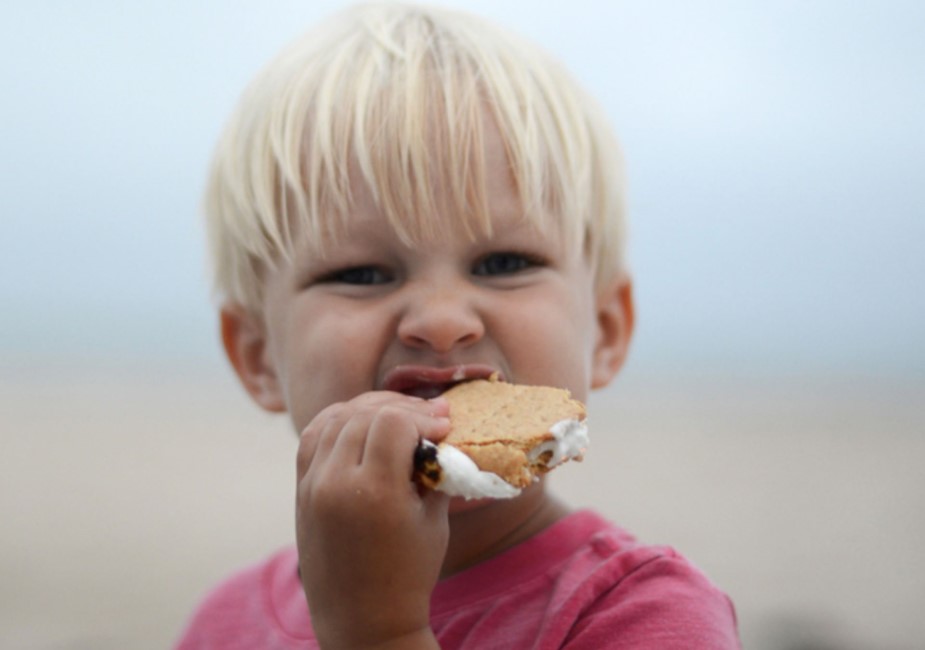 young blonde boy eating smores on the beach