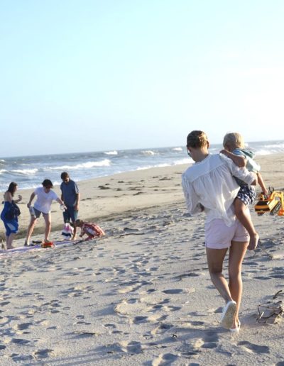 a young woman carries her toddler to a beach picnic