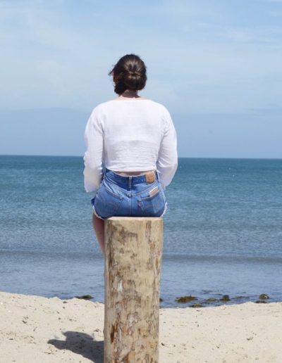 a young woman sits on a log and looks out to sea