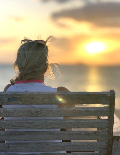 a woman watches the sunset on a bench in nassau