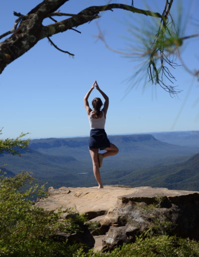 a young girl poses in a yoga pose at a look out point in australia