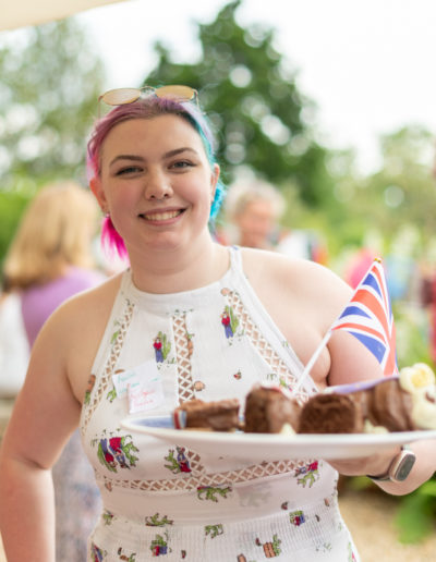 a young woman in a summer dress holds a jubilee cake