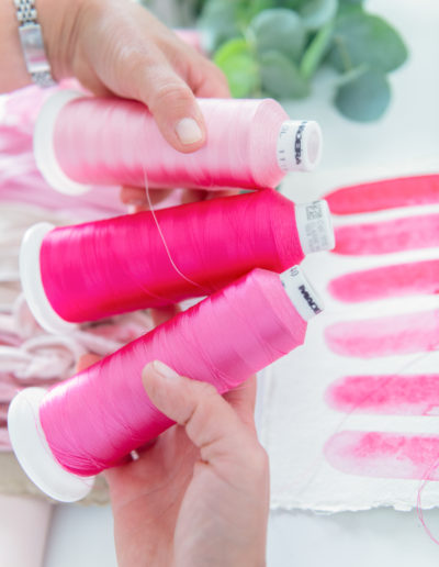 a woman holds three spools of pink cotton