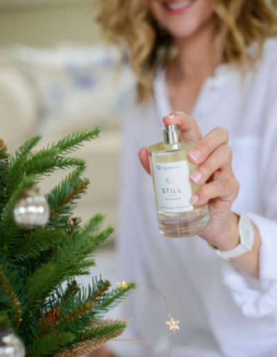a woman sprays scented mist onto a christmas tree during a personal branding photography shoot in surrey