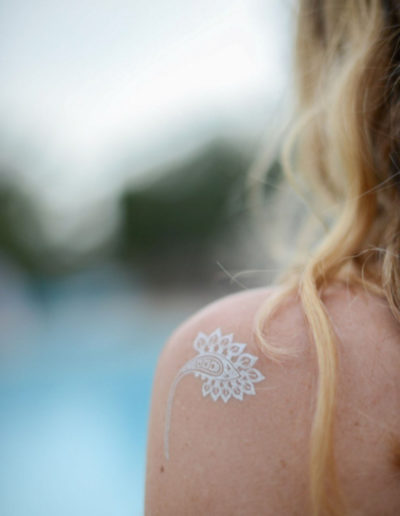 a woman sitting by a pool with a silver temporary tattoo