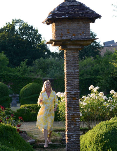 a woman in a yellow dress walks through a walled garden at sunset