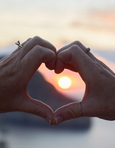 a woman makes a heart sign with her hands around a setting sun