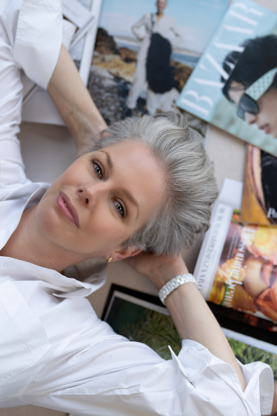 a silver haired woman lies amongst fashion magazines during a personal brand photography shoot in guildford