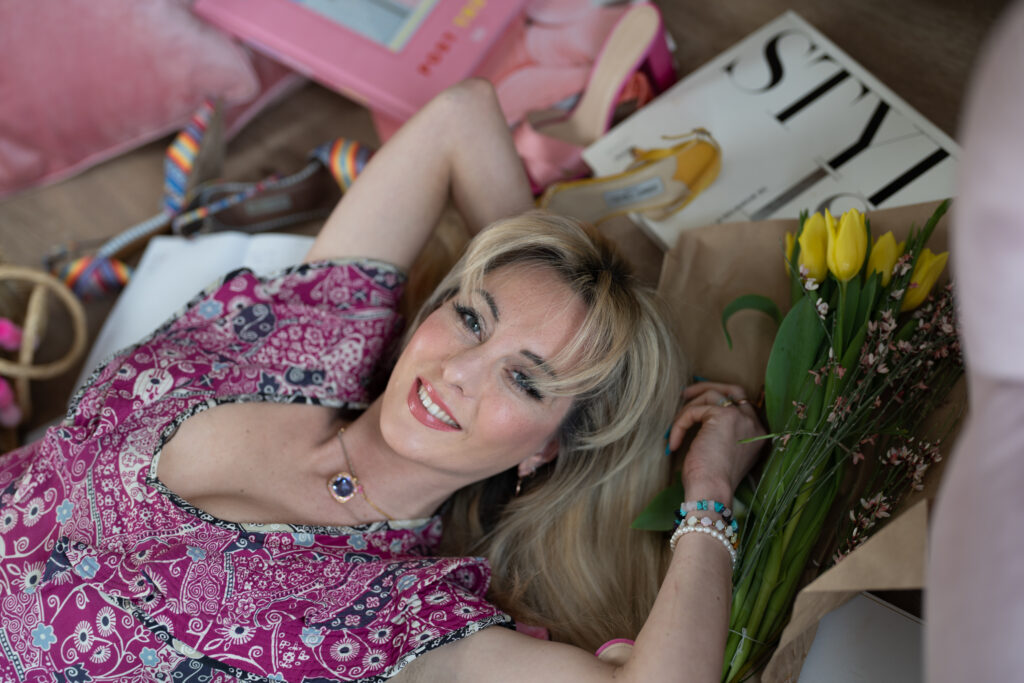 a young woman in a pink dress lying down amongst fashion magazines and flowers during a personal brand photography shoot in guildford