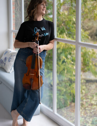 a musician leans against a large window holding her violin