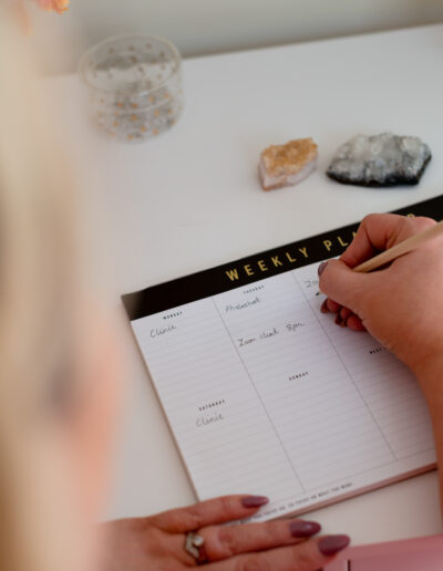 a woman makes notes in her weekly planner at her desk