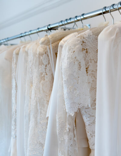 a row of designer bridal gowns hanging in a bespoke bridal studio