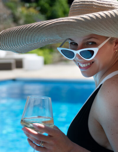 a woman wearing a large sun hat and glasses sits poolside during a personal brand photo shoot in surrey