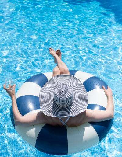 a woman in a large hat sits in a rubber ring in a pool during a personal brand photo shoot in surrey
