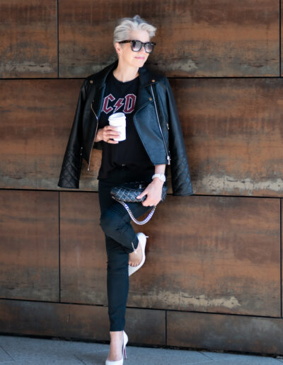 a woman wearing rock chick clothing leans agains a wooden backdrop for a personal brand photo shoot