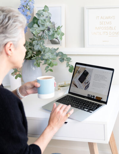 a woman sits at her computer desk with a coffee during a personal brand photo shoot