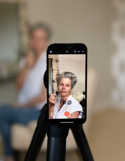 a woman films her makeup tutorial on an iphone during a personal brand photo shoot in surrey