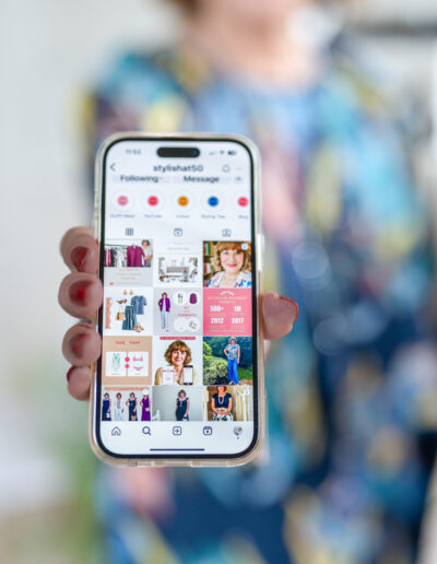 a woman holds up her phone with its instagram page during a personal brand photo shoot in surrey